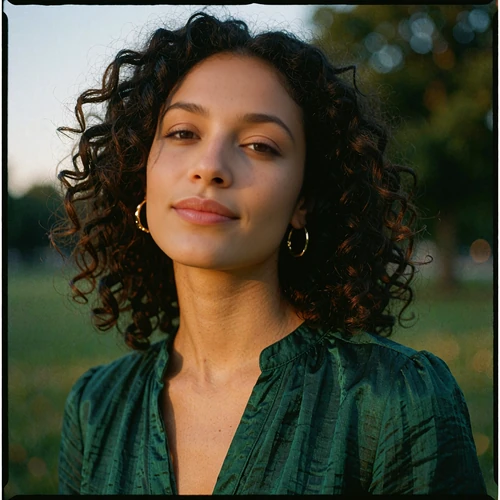 Young woman with dark curls and gold hoop earrings in evening park light, illustrative Orlando member avatar